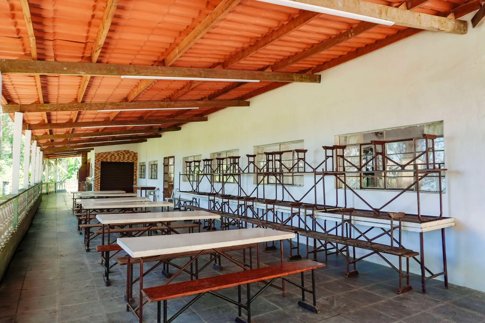 Refeitório coberto com mesas e bancos compridos de madeira